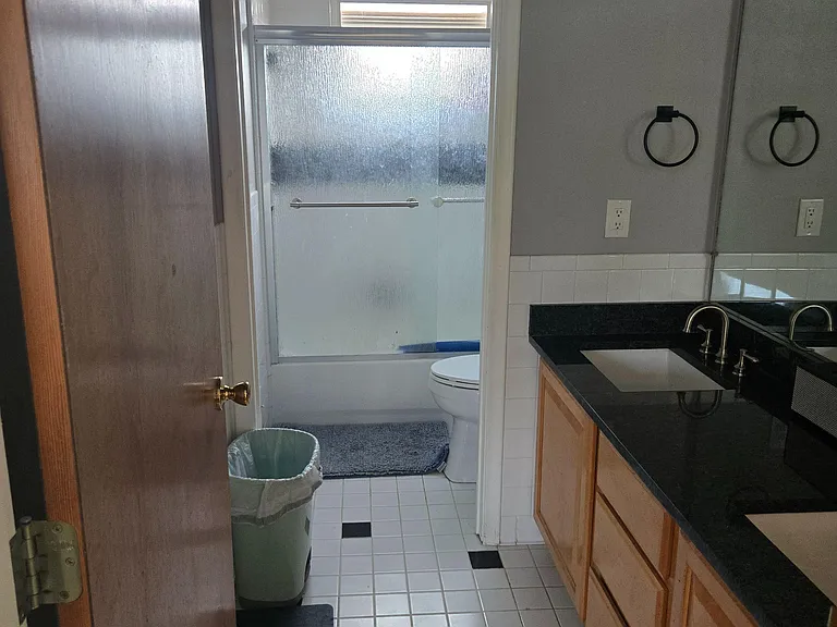 Full bathroom with tub/shower combo, tiled flooring, and a long vanity with sink and mirror for daily routines.