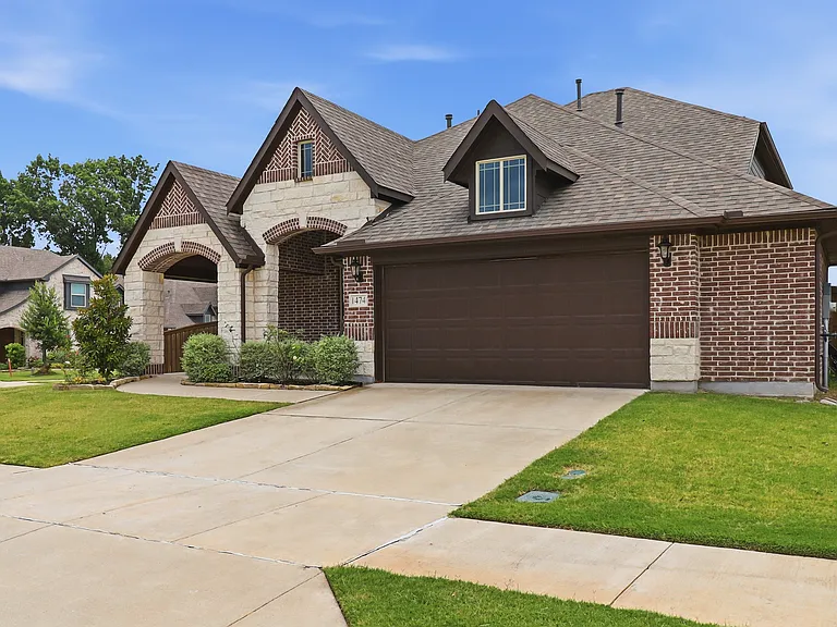 Brick and stone facade featuring arched portico entries, a 2.5-car garage with a brown door, and a dormer window