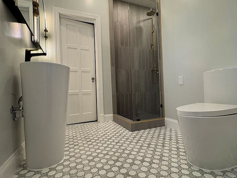 Jack & Jill bathroom. With large shower adorned with luxury, concrete tiles. Mosaic marble flooring and high-end lighting (Knurled brass fixtures above double sinks and lotus leaf brass chandelier.)