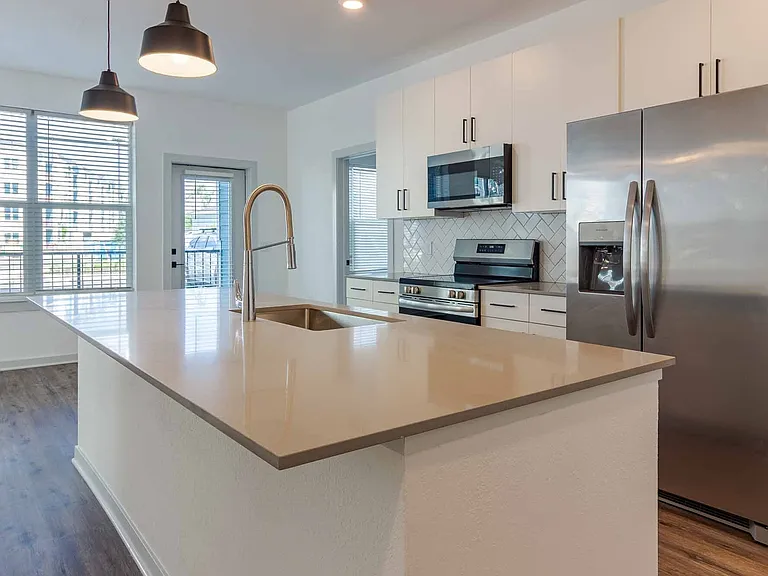 Open kitchen featuring a large quartz island, stainless steel appliances, white cabinetry, and a herringbone tile backsplash. Open kitchen featuring a large quartz island, stainless steel appliances, white cabinetry, and a herringbone tile backsplash.