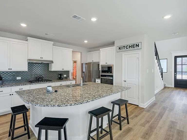 Contemporary kitchen featuring a large island with granite countertops, white cabinetry, a dark tile backsplash, stainless steel appliances, and wood-finish flooring