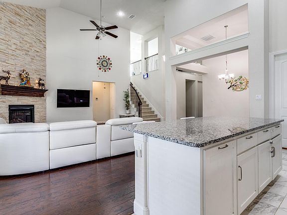 Kitchen featuring a stone fireplace, high vaulted ceiling, ceiling fan with notable chandelier, white cabinetry, and dark wood-type flooring