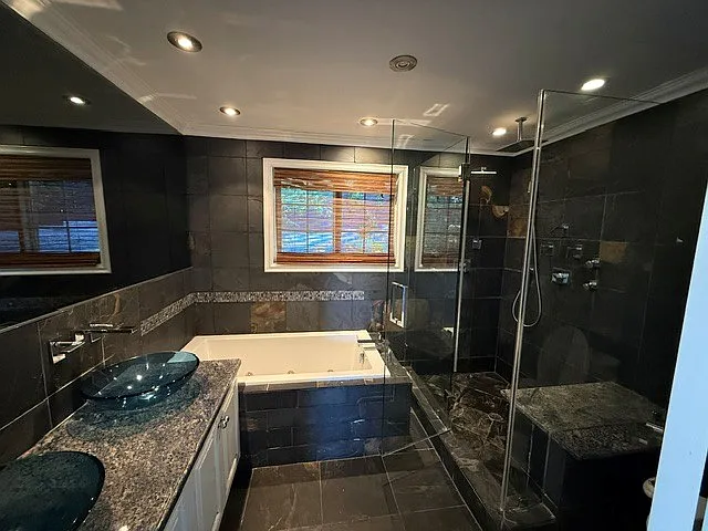 Master bedroom bath with jacuzzi tub, rain shower, granite countertop, and stone tile.