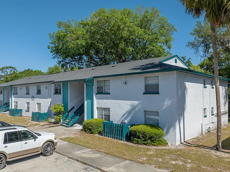 Charming white and teal apartment building surrounded by lush greenery and palm trees, offering a serene living environment.