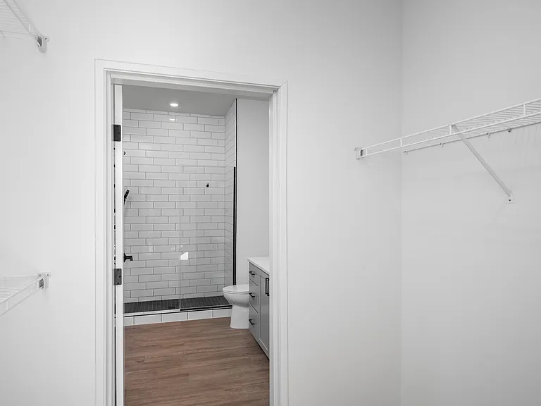 Sleek modern bathroom with subway-tiled shower and adjacent spacious walk-in closet, featuring clean design and elegant wooden flooring. Sleek modern bathroom with subway-tiled shower and adjacent spacious walk-in closet, featuring clean design and elegan