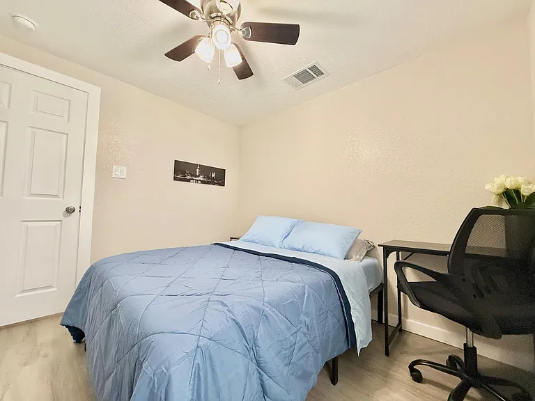 Furnished bedroom with ceiling fan, comfortable bed, and a dedicated desk area for work or study.