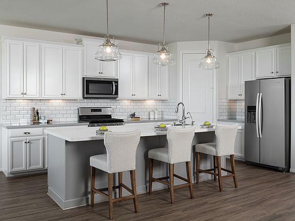 The kitchen features a large center island with walk in pantry with white cabinetry, quartz countert