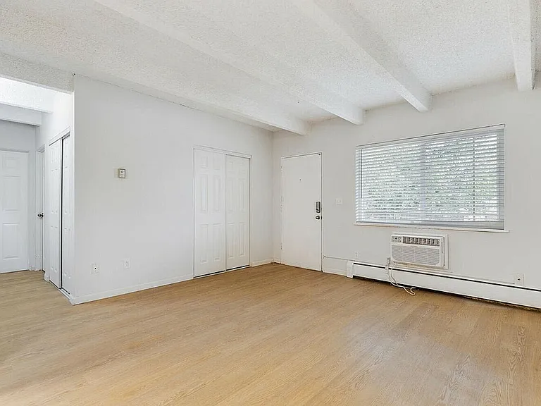Bright and airy living space with sleek wooden floors, white walls, and a large window featuring a view of greenery.