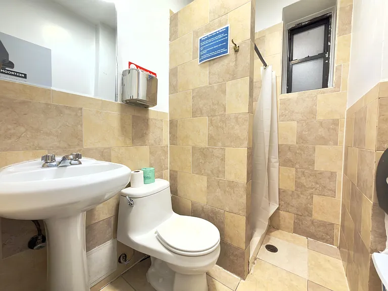 Tiled bathroom with walk-in shower, pedestal sink, and frosted window for ventilation and privacy.