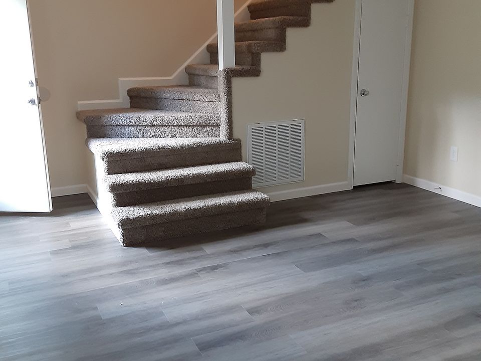 Your standing in living room with new carpeted stairs that lead to 2 bedrooms, 1 new bath with all new fixtures. All new living room, with new window, flooring, paint, hot water heater with new front door is open.