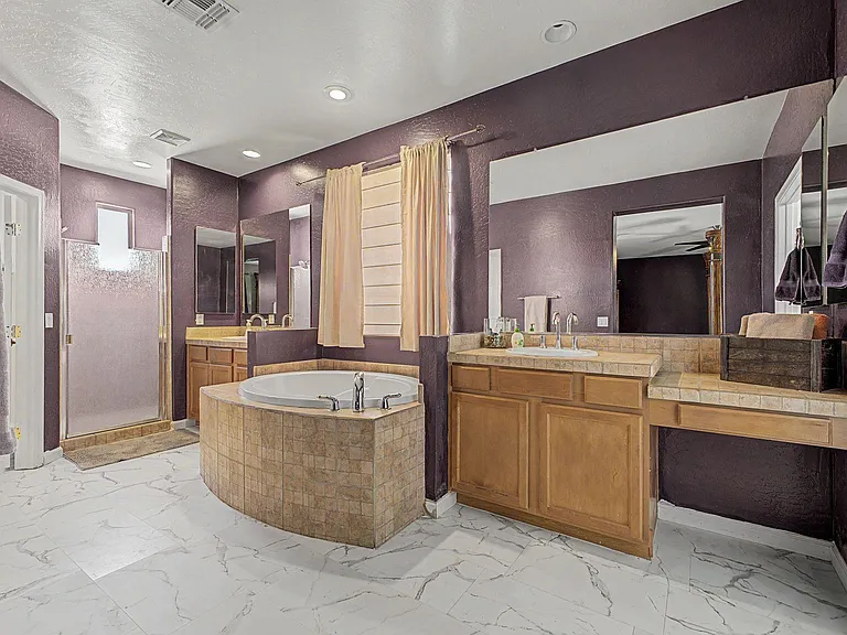 Spacious bathroom with dual-sink vanity, large mirrors, tiled countertops, and a soaking tub plus separate shower.