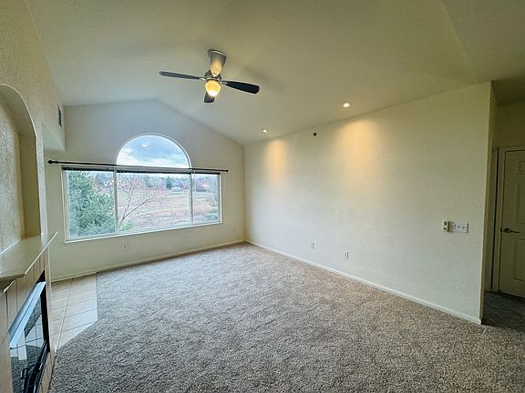 The living room has a ceiling fan and large windows overlooking open space