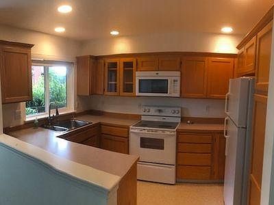 Kitchen with white appliances & large pantry. Dishwasher opposite side of stove/oven/microwave. Warm canned lighting. Double stainless steel sink with retractable faucet & spray nozzle. Note countertop for barstools.