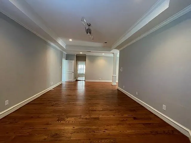Spare room featuring dark wood-type flooring, crown molding, a tray ceiling, recessed lighting, and ornate columns