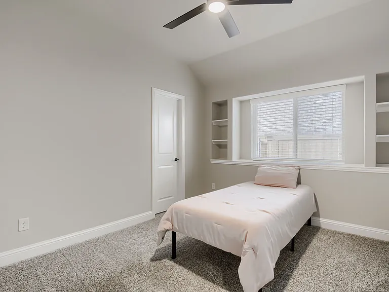 Carpeted room with a modern ceiling fan, a window featuring blinds, and integrated shelving units