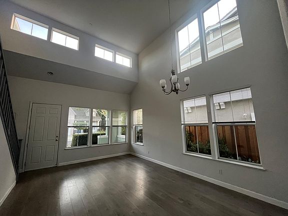 Spacious living room with soaring high ceiling, recessed lighting, laminate flooring and multiple windows filling the space with natural light.