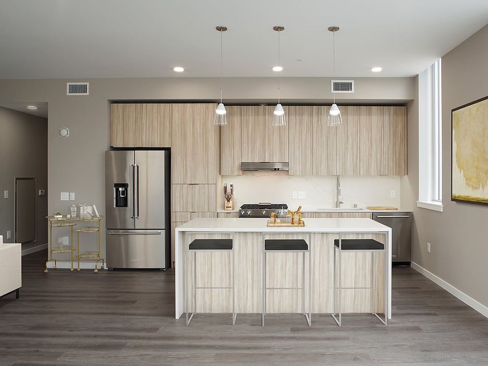 Signature Collection penthouse kitchen with oak cabinetry and undercabinet lighting, white quartz countertops and backsplash, upgraded stainless steel appliances, and hard surface flooring.