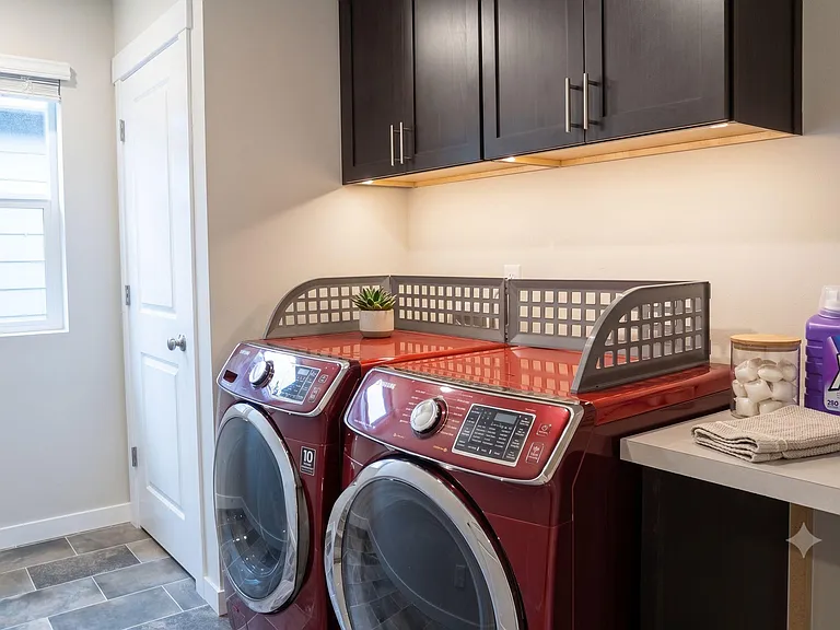 Dedicated laundry area with full-size front-load washer and dryer, upper storage cabinets, and a convenient folding counter.