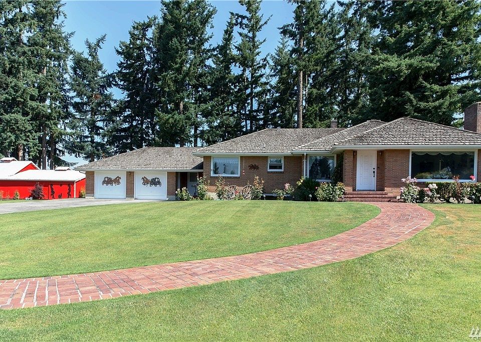 Brick path leading up to striking brick home with cedar shake roof! Barn/workshop to the left, double car garage, separate covered entrance from garage leading into office or kitchen. Large picture window in living room helps keep home bright inside1