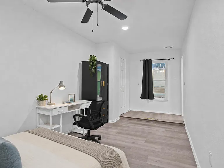 Spacious bedroom with wood-look flooring, ceiling fan, and a dedicated desk area plus wardrobe storage.