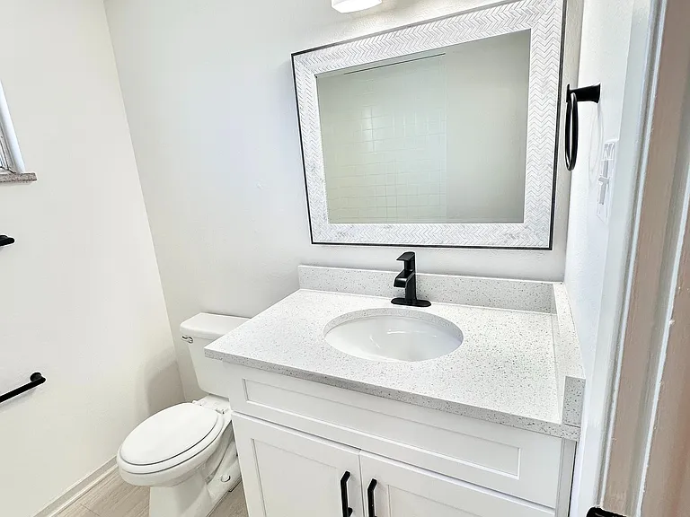 Modern bathroom with sleek white vanity, elegant mirror, and stylish lighting fixtures.
