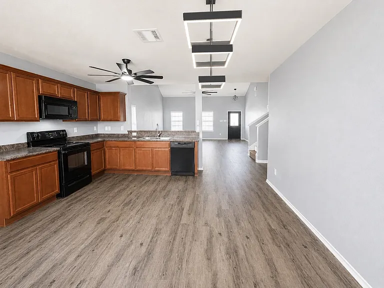 Open-concept kitchen featuring wood-finish cabinetry, dark countertops, and black appliances