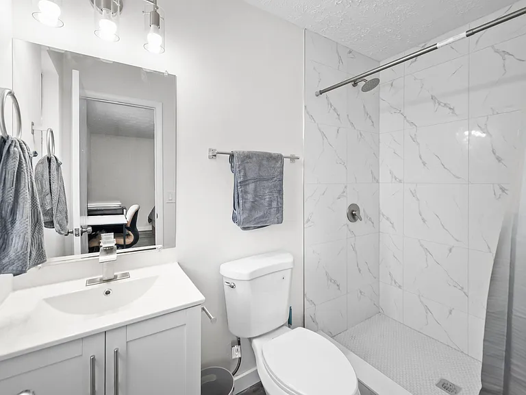 Updated bathroom with a single-sink vanity, wall mirror, and a walk-in shower with large-format tile surround.