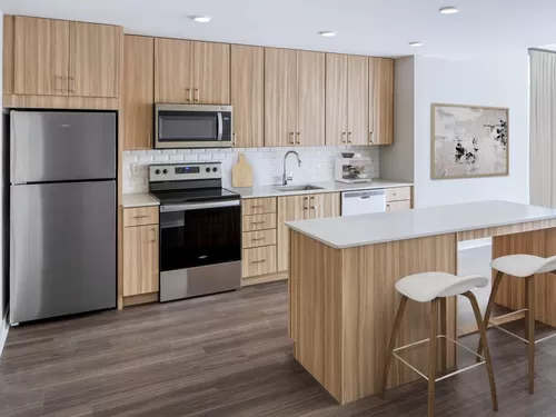Finish Package I Kitchen with oak cabinetry, white tile backsplash, white quartz countertops, and stainless steel appliances (Representative photo) - Avalon Bothell Commons
