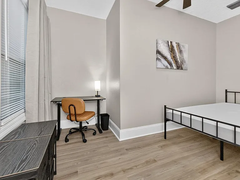 Bedroom offers a dedicated desk workspace, ceiling fan, and wood-look flooring with a window for natural light.