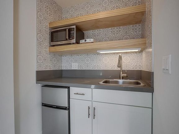 Modern kitchenette with mini fridge, microwave, sink and hot plate.