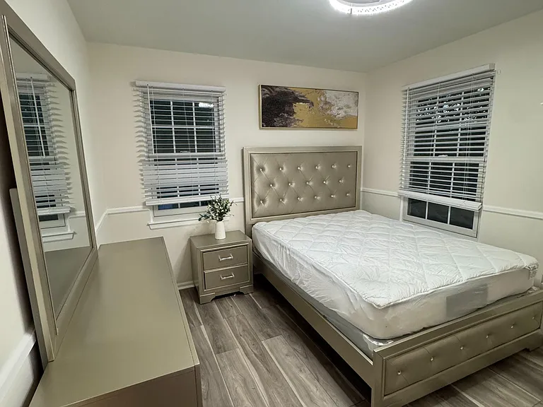Furnished bedroom with two windows, a tufted bed, and matching dresser and nightstand, plus durable wood-look flooring.