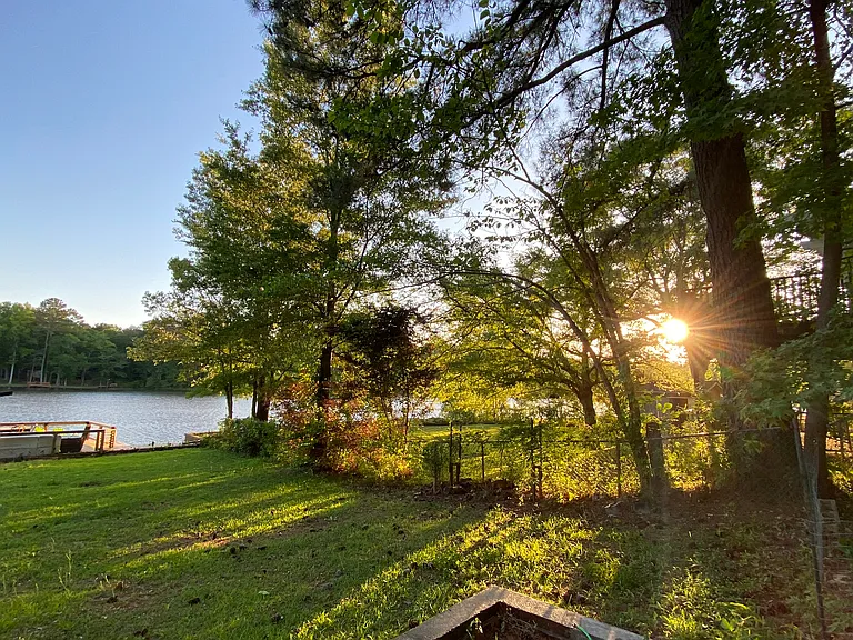 Lakeside backyard with string lighting, dock, firepit, and sunset views.