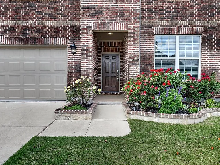 Brick facade residence featuring a paneled garage door, a dark wood entry door, and a white-framed window