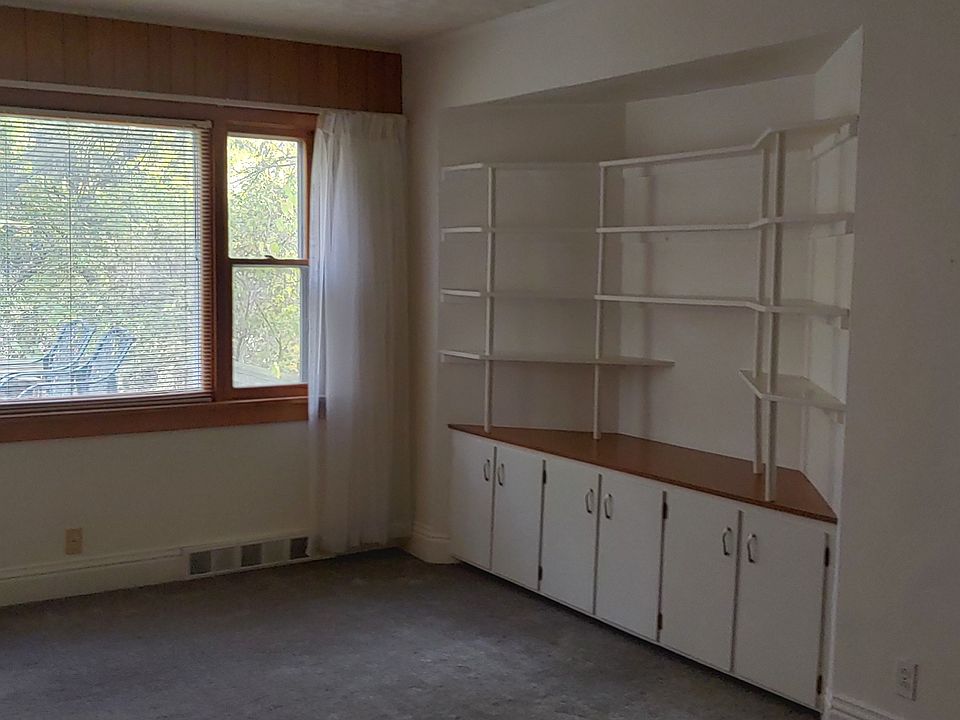 Livingroom with picture window, custom built in book shelves / TV shelf with lots of cabinet storage below. To right, front door going out to front porch.