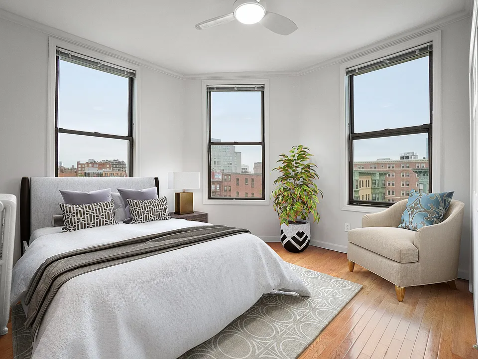 Bright and airy bedroom with three large windows, offering stunning city views, stylish decor, and a comfortable lounge chair.