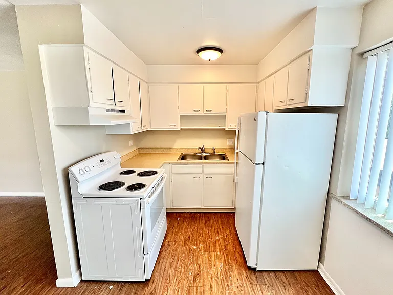 Charming kitchen with modern white cabinetry, efficient appliances, and warm wood-style flooring.
