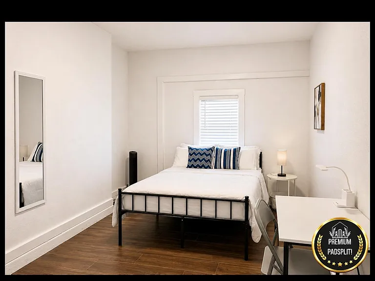 Furnished bedroom with a full bed, work desk, and window blinds for privacy and natural light.
