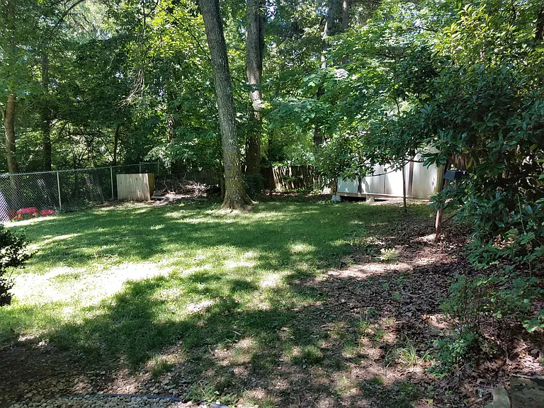 Shady fenced in backyard with garden shed and stone firepit.