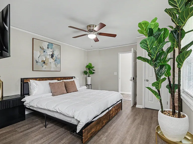 Spacious bedroom with a comfortable bed, ceiling fan, and TV, plus window blinds and wood-look flooring for easy upkeep.