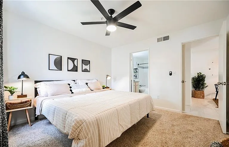 Spacious bedroom with plush carpeting, ceiling fan, bedside lighting, and easy access to an adjacent bath.