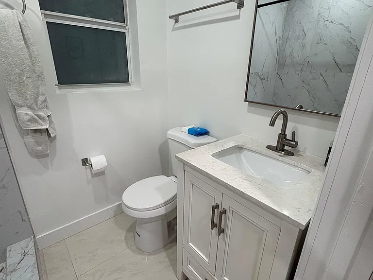 Updated bathroom with a quartz-top vanity, under-sink storage, large mirror, and tile finishes for easy upkeep.