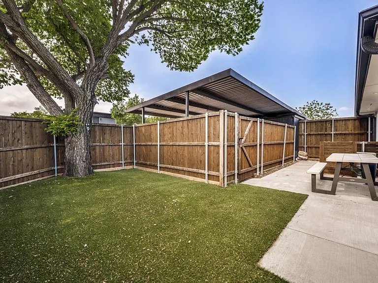 Fenced backyard with artificial turf, mature tree, and concrete patio