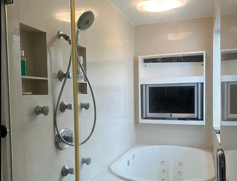 Multiple shower heads and a deep jacuzzi tub for two with TV in primary suite.