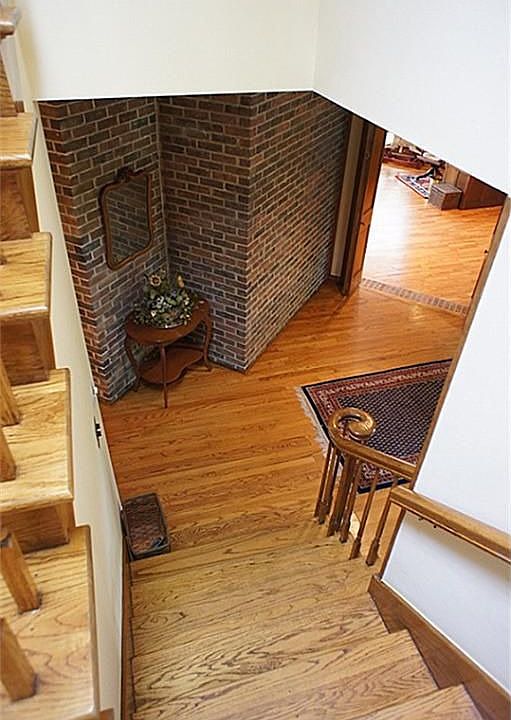 A view down the wooden stairway, featuring a brick accent wall in the foyer