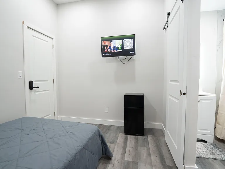Private bedroom with wood-look flooring, mounted TV, and convenient access to an adjacent bathroom with shower/tub.