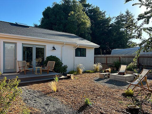 Yard features fire pit, garden beds, deck, outdoor lounge chairs.