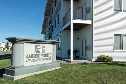 The exterior of Amber Pointe with an outside monument and views of the deck and patio. - Amber Pointe Apartment Homes