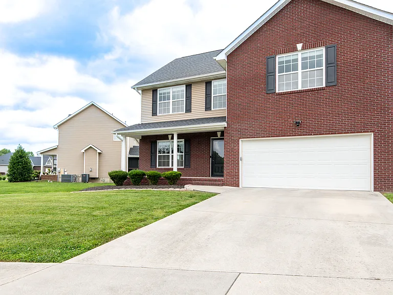Front of property features, yard driveway, mulched area with bushes, covered porch and sidewalks