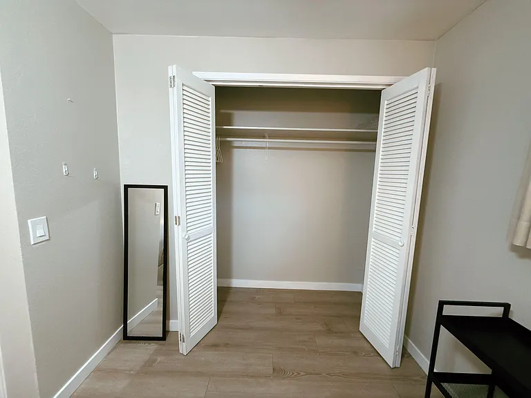 Bedroom closet with double louvered doors, hanging rod, and upper shelf for organized storage.