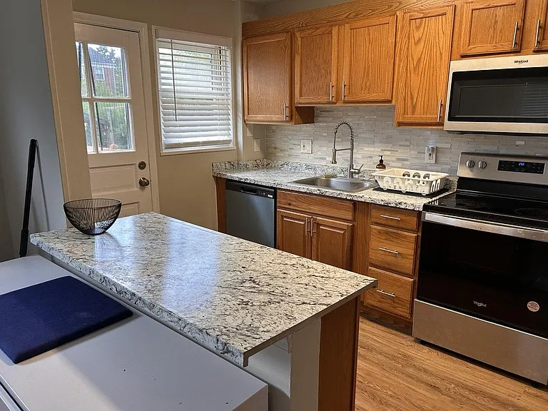 Kitchen offers ample wood cabinetry, granite-look counters, stainless appliances, and a breakfast bar plus exterior door acce